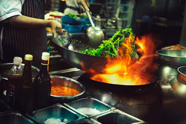 A chef tosses kale in a wok over an open flame.
