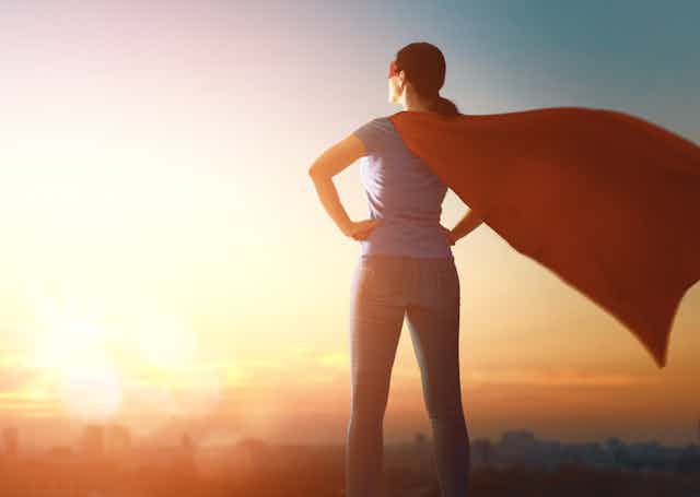 back of a woman standing with hands on hips and superhero cape
