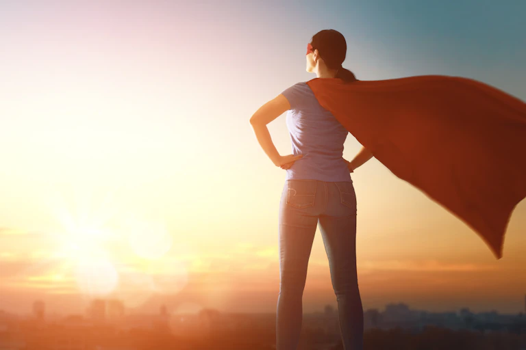 back of a woman standing with hands on hips and superhero cape