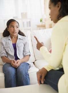 girl seated on couch gets lecture from a woman