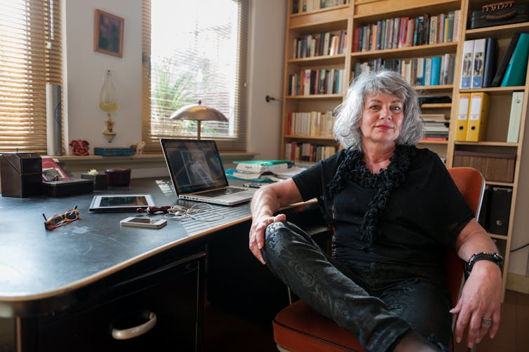 woman seated at her desk smiles with her legs open and arms wide on arm rests