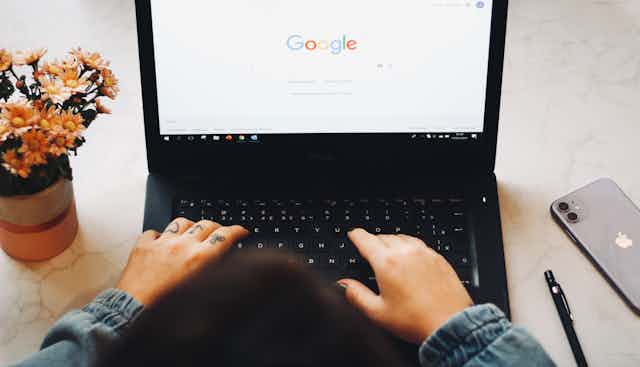 hands with tattoos and painted nails on a laptop keyboard with the screen showing the Google search homepage