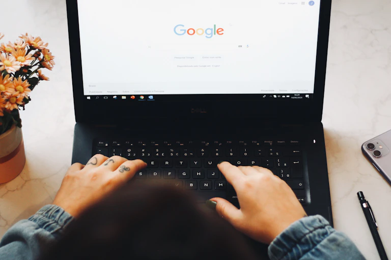 hands with tattoos and painted nails on a laptop keyboard with the screen showing the Google search homepage