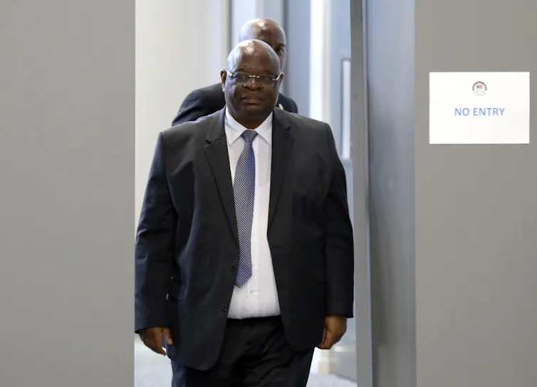 A bald man wearing a tie and suit walks into a room.