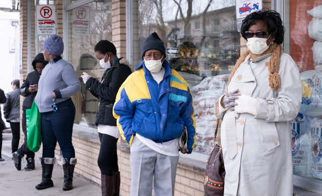 Des gens portant le masque font la queue devant une épicerie