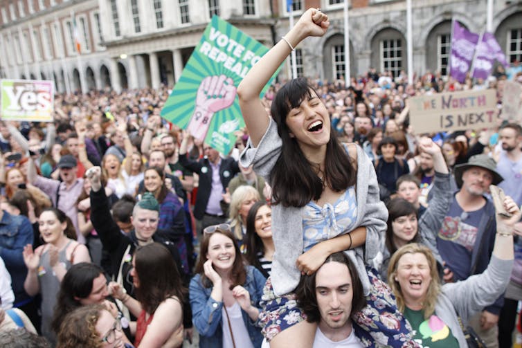 A group of people smile, cheer and wave signs in celebration