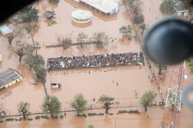 People crowd together on an exposed building in the centre of brown floodwater