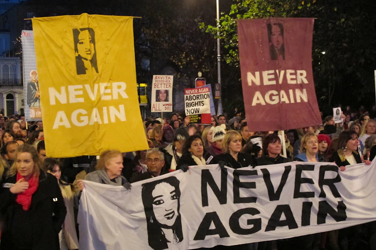 A crowd marches holding signs saying 'never again' and photos of a woman.