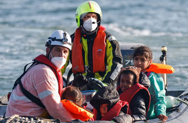 Two men wearing life jackets and masks sit with small children in a motorboat at sea.