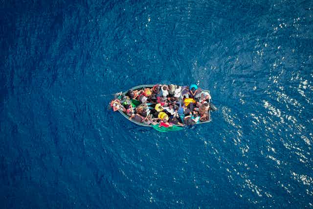 An aerial photo shows a small boat full of people in the middle of an ocean
