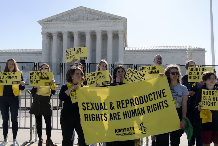 Women in front of the Supreme Court hold yellow signs that say "Sexual & reproductive rights are human rights."