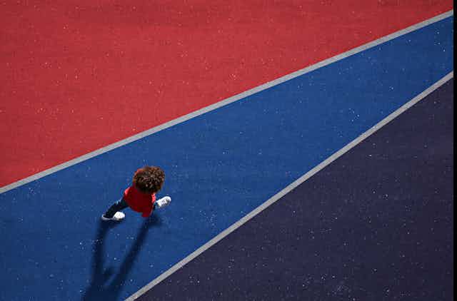 A boy walks on asphalt painted blue and red.