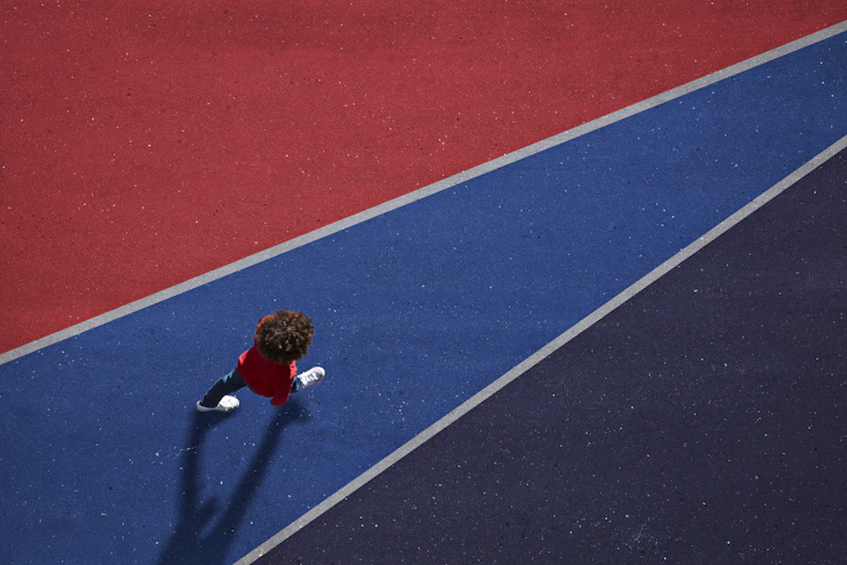A boy walks on asphalt painted blue and red.