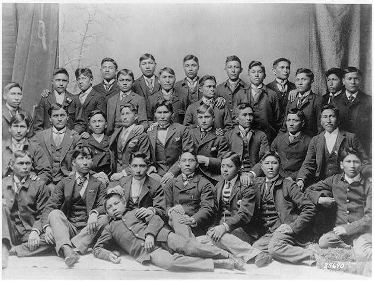31 young men in jackets and ties, some with vests, in a group photo in which none are smiling.