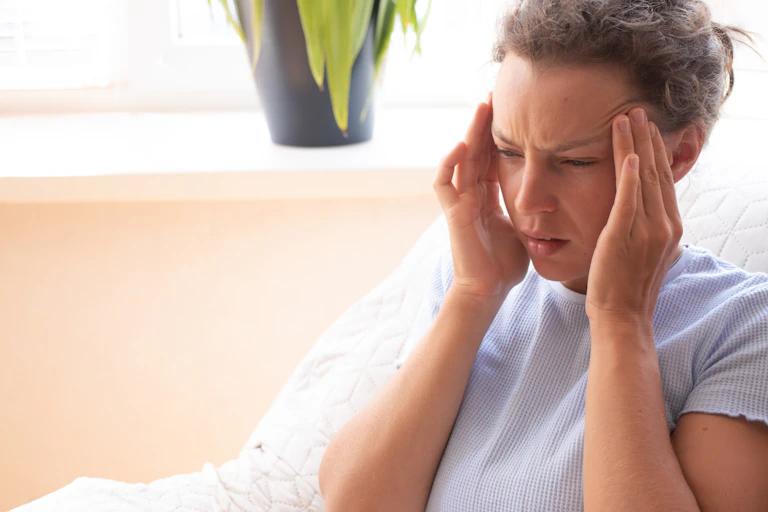 Woman holds the side of her head, squinting.