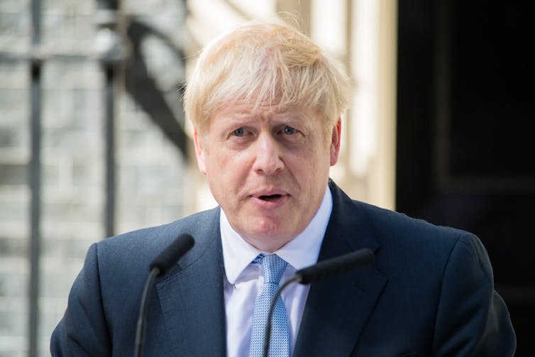 Boris Johnson in a blue suit pictured behind a lecturn outside.