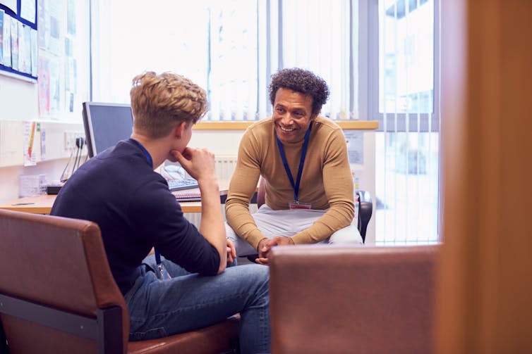 A professional sits with a young man in an office.