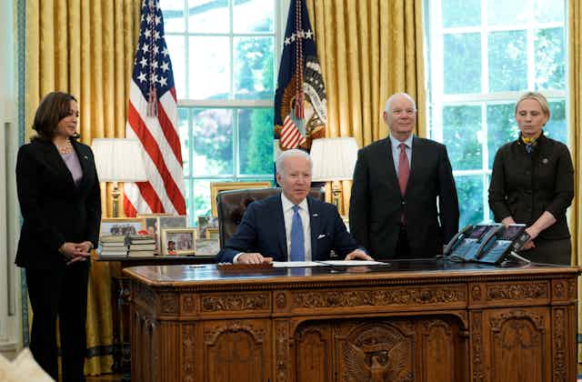 Joe Biden sits at his desk in the Oval Office of the White House flanked by aides