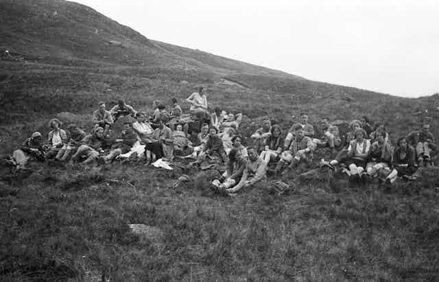 A black-and-white photo of young people sitting on a grassy mountainside.