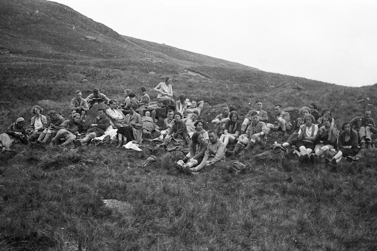 A black-and-white photo of young people sitting on a grassy mountainside.