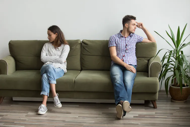 a man and woman sit on a green sofa turned away from each other.