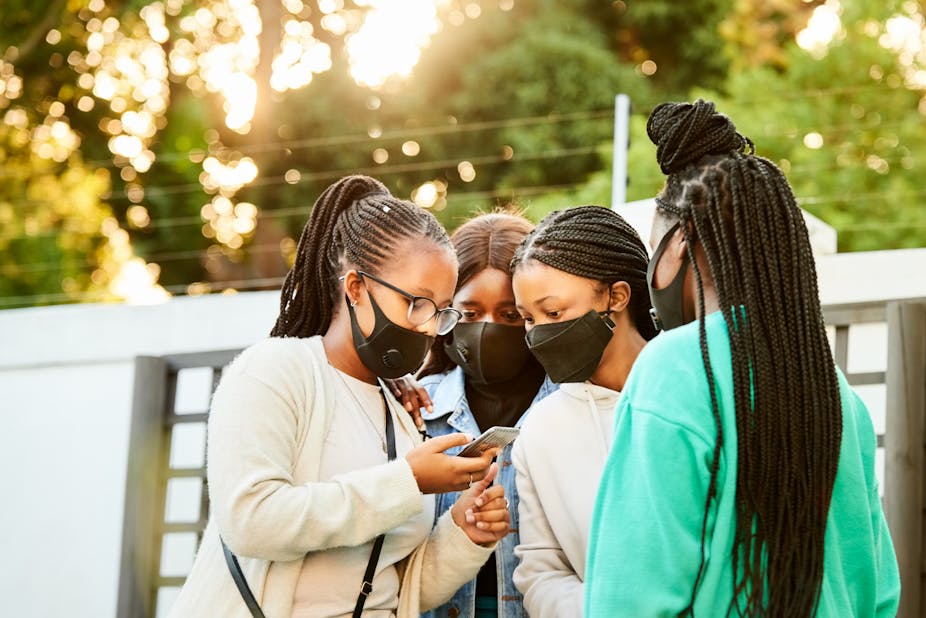 A group of girls wearing face masks looking at something on a mobile phone together.