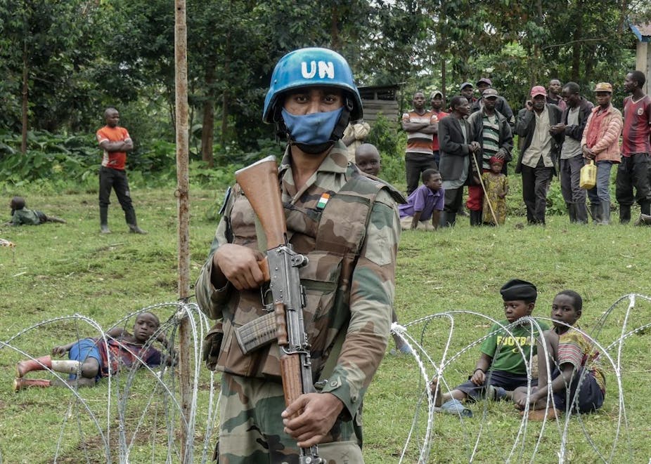 An armed peacekeeper stands guard over displaced civilians.