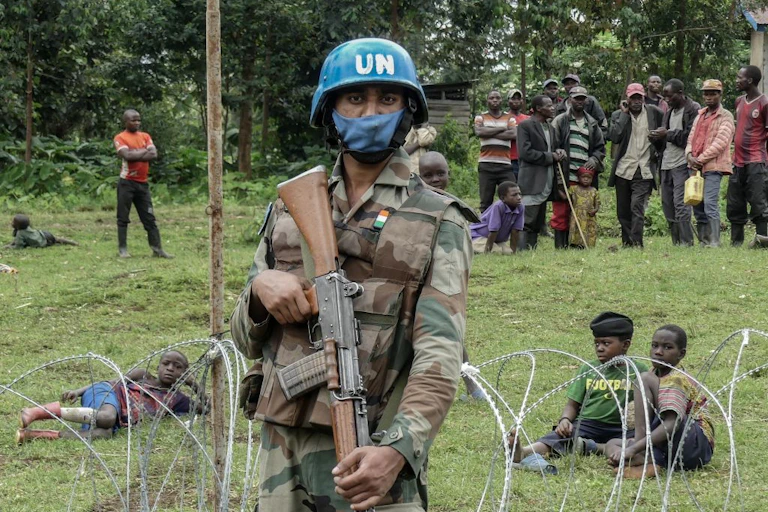 An armed peacekeeper stands guard over displaced civilians.
