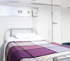 A bed with a purple checked bedspread is seen in a hospital.