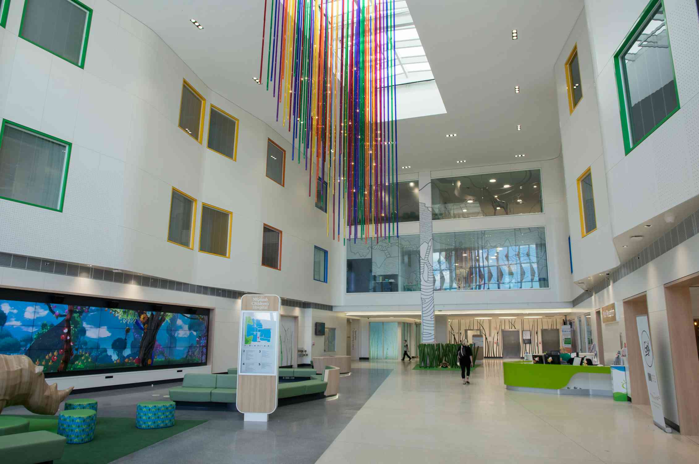 Colourful streams hang from a very high ceiling in a hospital foyer as a person walks through.