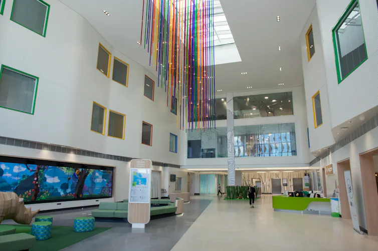 Colourful streams hang from a very high ceiling in a hospital foyer as a person walks through.