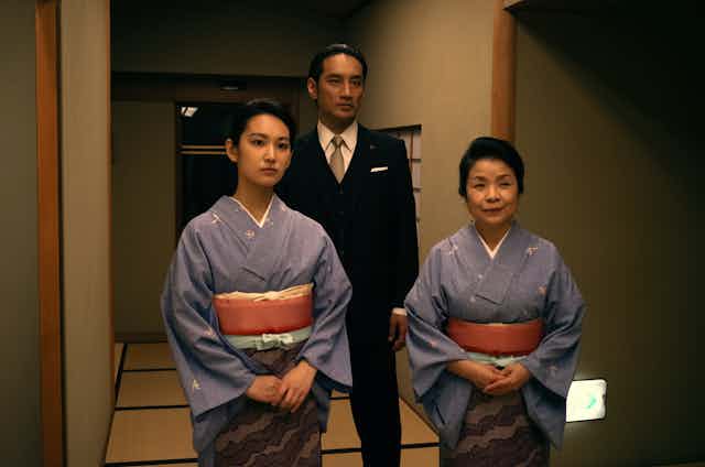 Man in suit behind two women in traditional Japanese dress.