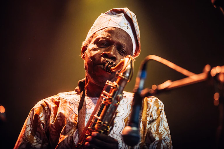 Man in traditional attire blowing the trumpet with a microphone in front of him