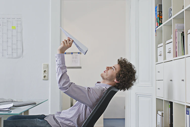 A man at a desk holding a paper airplane.