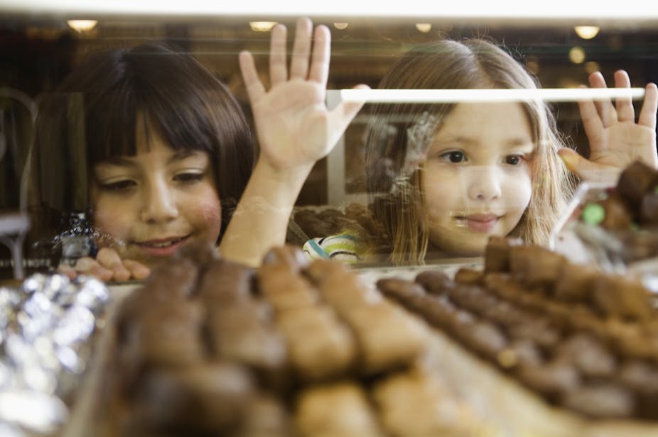 Two young girls looking at the display of chocolate through the store window.