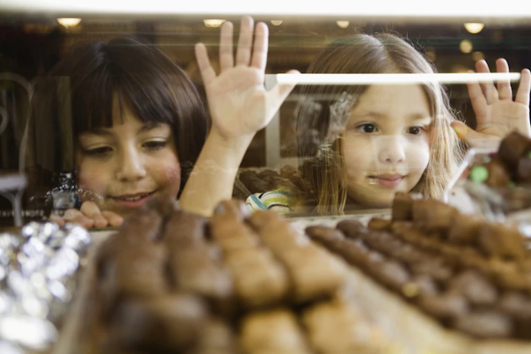 Two young girls looking at the display of chocolate through the store window.