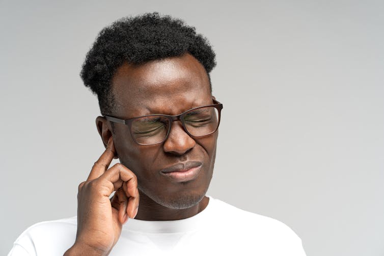 A man touches his ear, indicating pain.