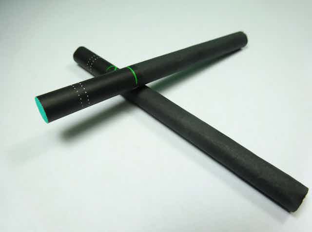 Two black cigarettes form an X against a very pale green background.