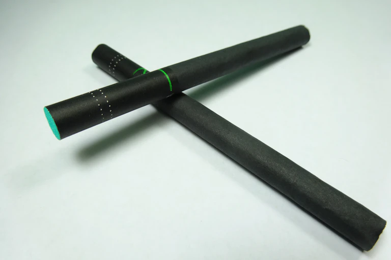 Two black cigarettes form an X against a very pale green background.