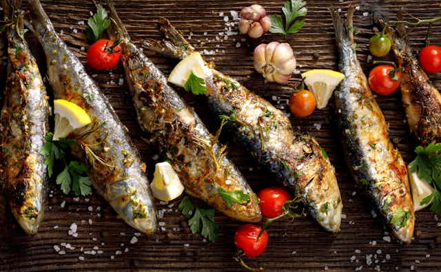 Fried sardines are places on a board with lemon wedges and tomato as garnish
