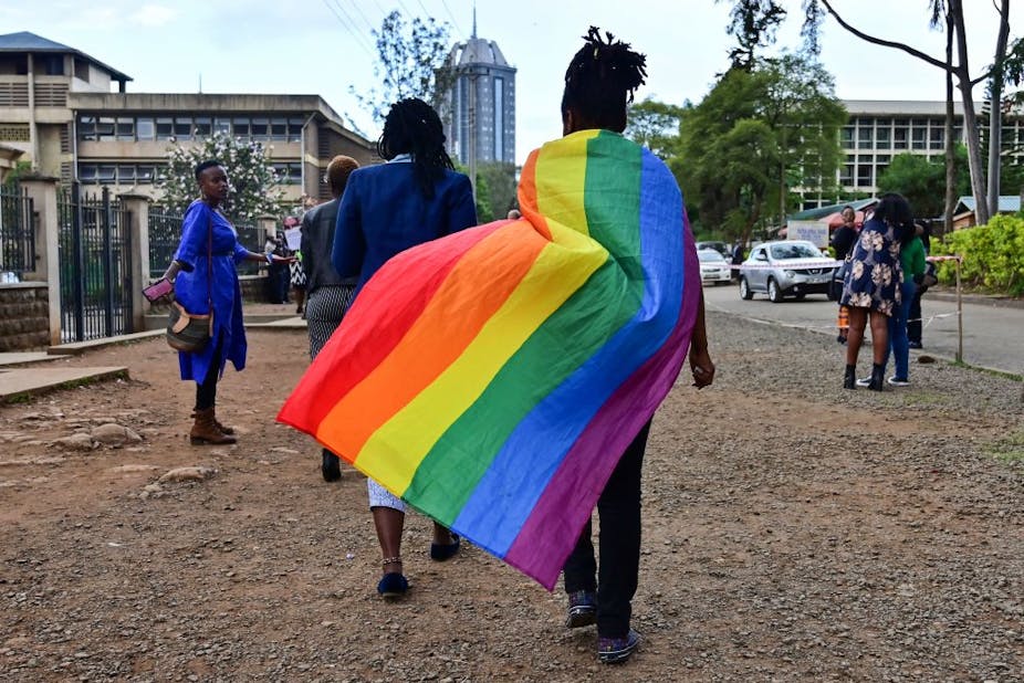 A person walks with a rainbow flag draped over their shoulders.