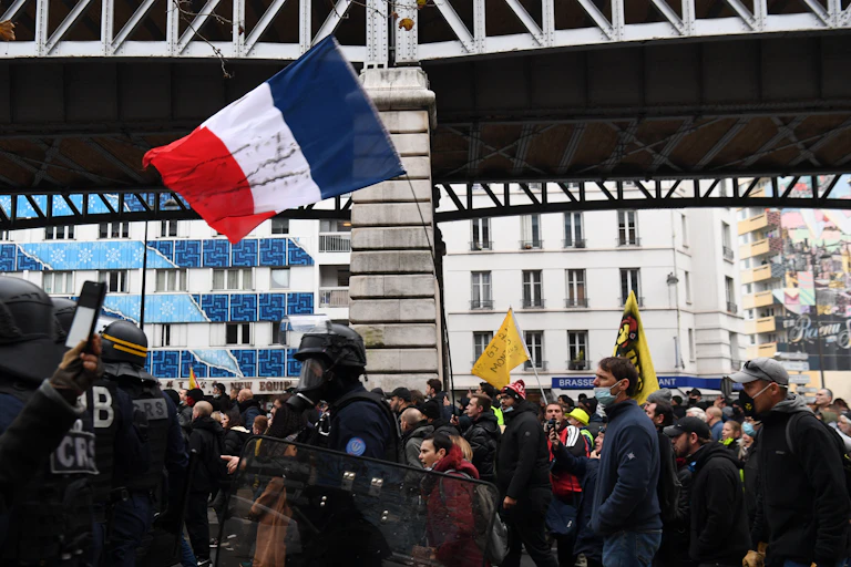Un manifestant brandit un drapeau national alors que des policiers anti-émeutes marchent parmi les manifestants lors d'une manifestation de Gilets Jaunes à Paris, le 20 novembre 2021.