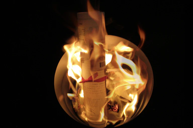 A black background with a bowl in the centre, documents are burning