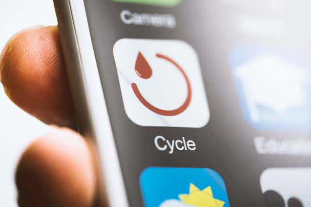 close-up of a smart phone screen in a person's hands showing an app icon of a red drop of liquid and a red semicircle