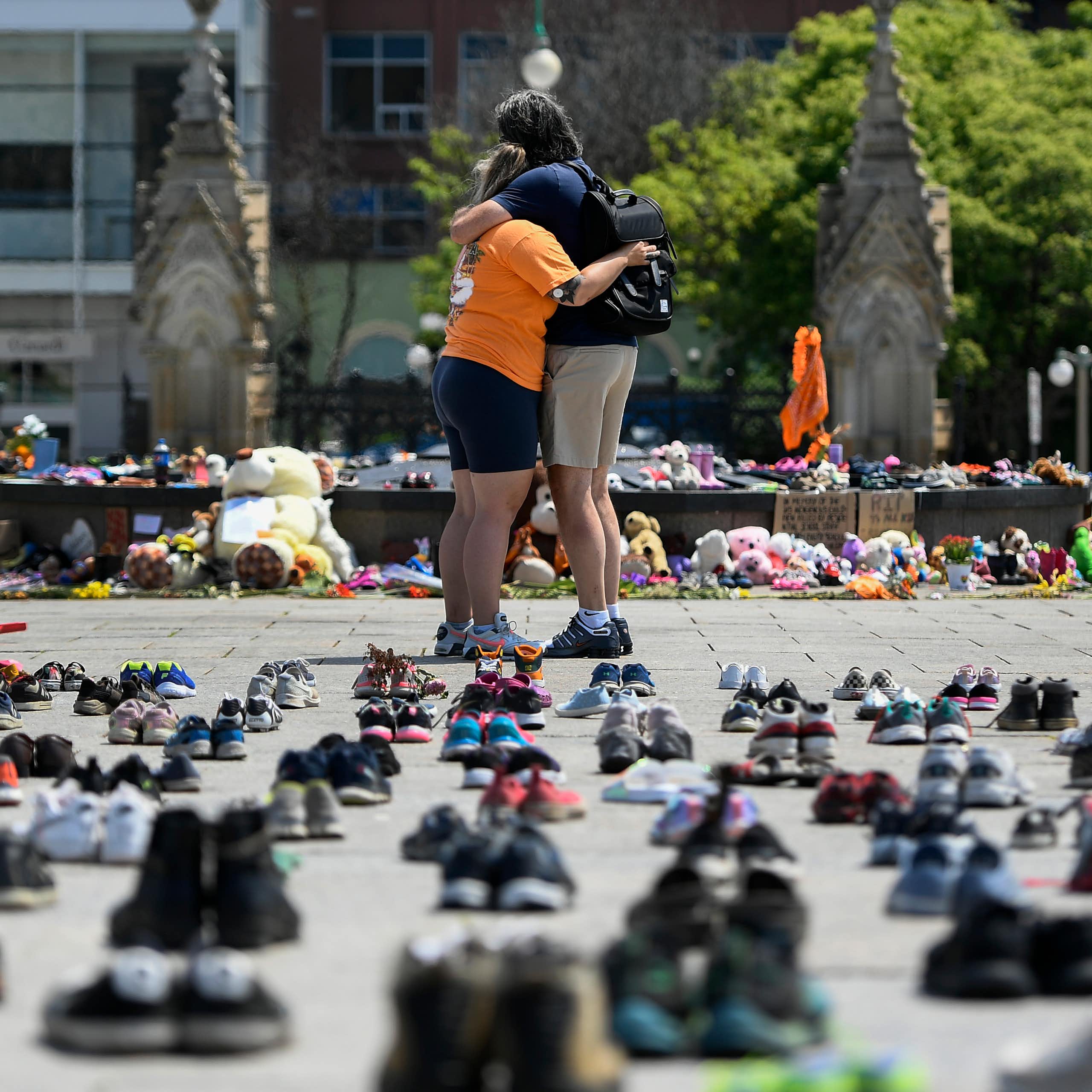 One of the two people outside the Parliament Hill is wearing an orange shirt to honour the 215 Indigenous children. The background has shoes, toys and children's clothes as a sign of remembrance. 