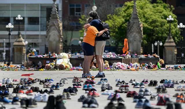 One of the two people outside the Parliament Hill is wearing an orange shirt to honour the 215 Indigenous children. The background has shoes, toys and children's clothes as a sign of remembrance. 