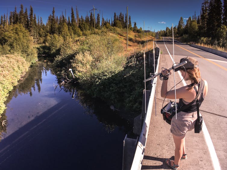 a woman stands on the side of a bridge aiming at the river below