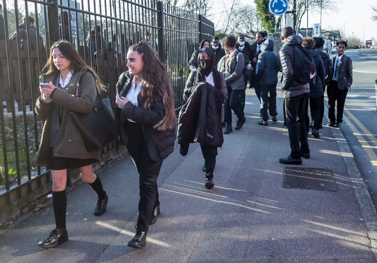 Secondary-school pupils in uniform walk out of school grounds.