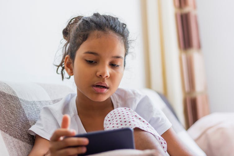 A girl watches a smartphone screen.