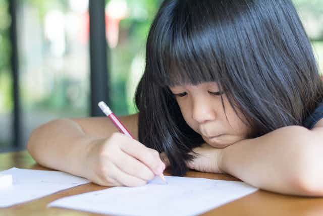 Young girl writing on sheet of paper with pencil